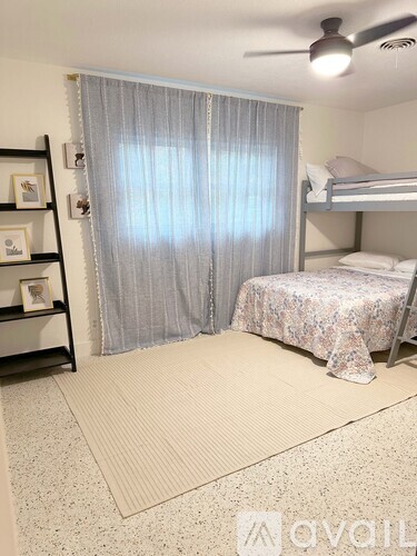 A bedroom with a bed, a fan, and a window with curtains.