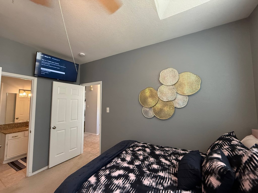 A bedroom with a bed, a mirror, and a TV mounted on the wall.