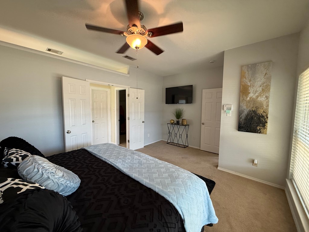A bedroom with a bed, a ceiling fan, and a painting on the wall.