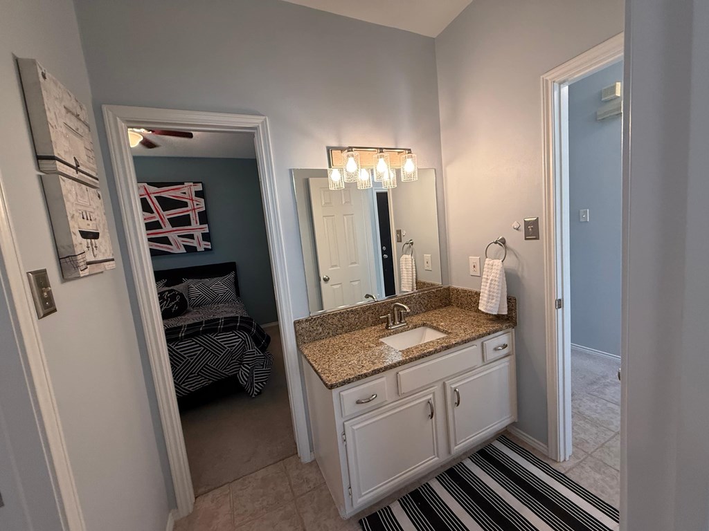 A bathroom with a sink, mirror, and a bed in the background.