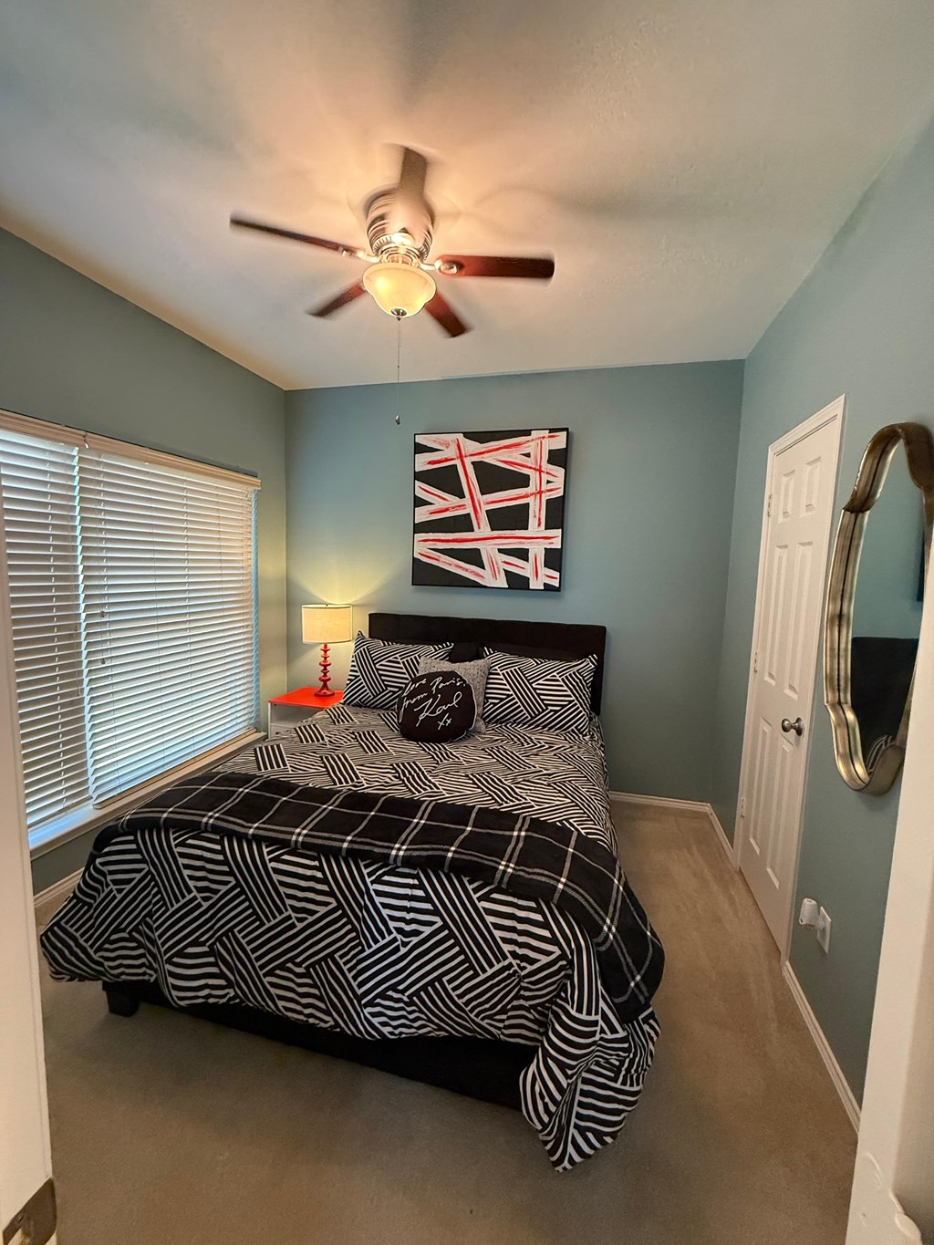 A bedroom with a bed, a ceiling fan, and a mirror.