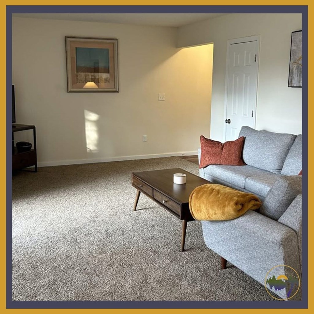 A living room with a grey couch, a coffee table, and a painting on the wall.