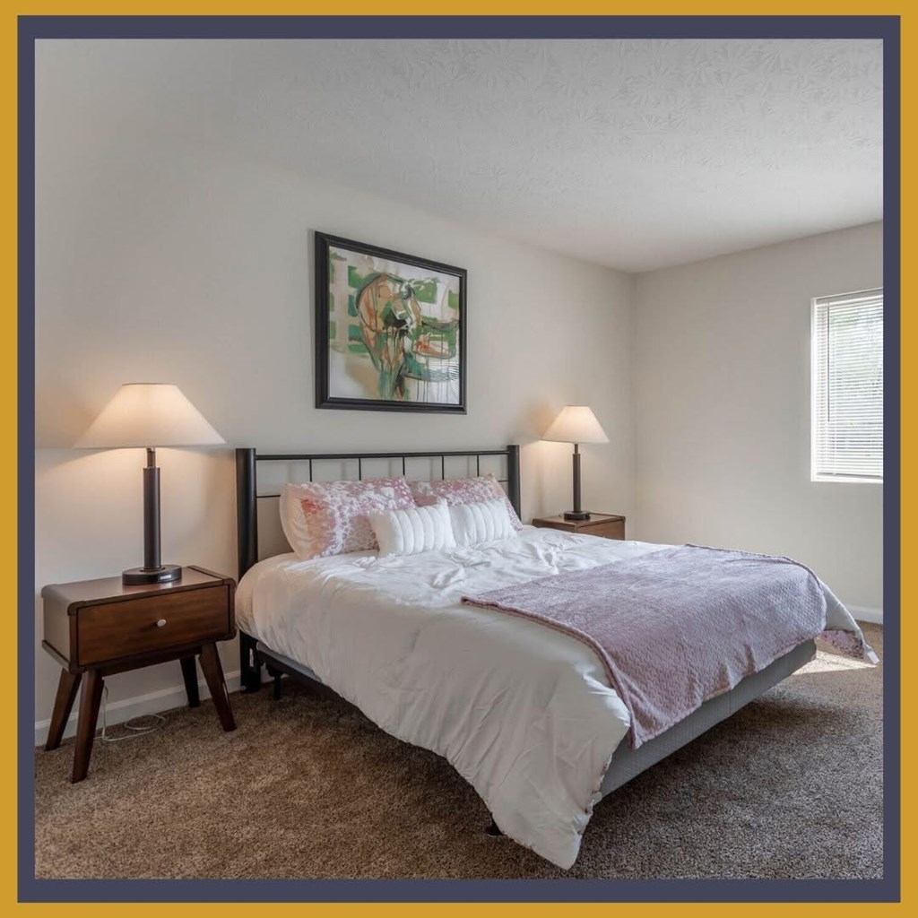 A bedroom with a bed, two lamps, and a painting on the wall.
