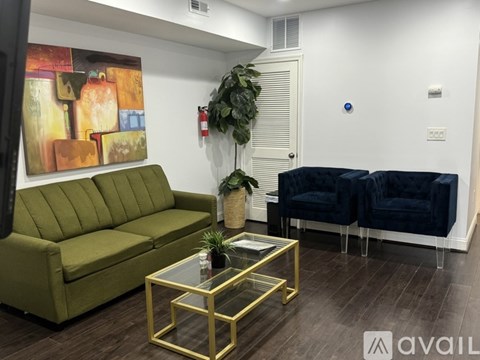 A living room with a green couch, a glass table, and a painting on the wall.