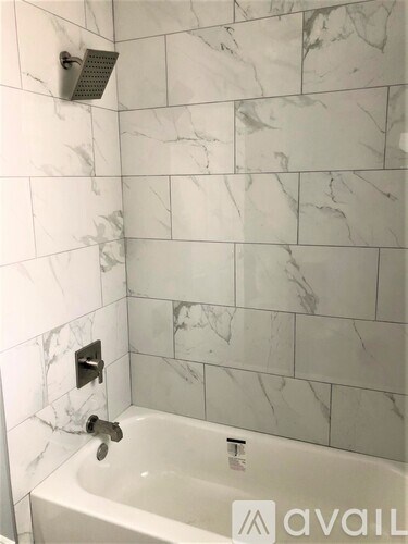 A bathroom with a marble tile wall and a white bathtub.