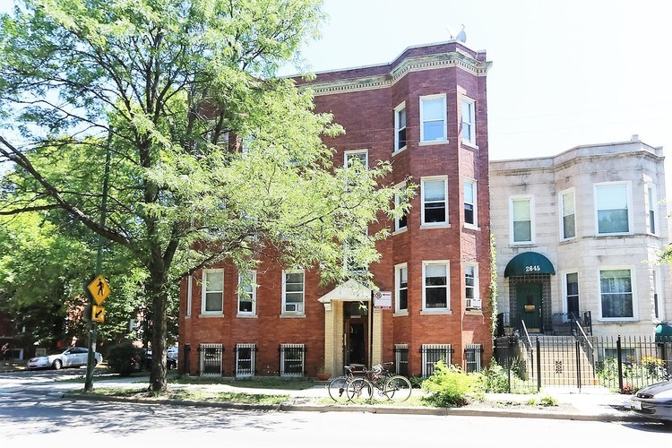 A red brick building with a green awning sits on a street corner.