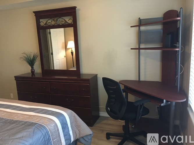 A bedroom with a bed, desk, chair, and a mirror.