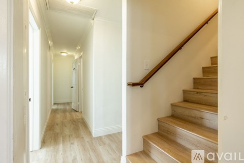 A hallway with wooden floors and a staircase with wooden steps and handrail.