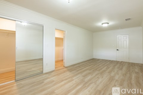 A spacious room with wooden flooring and white walls.