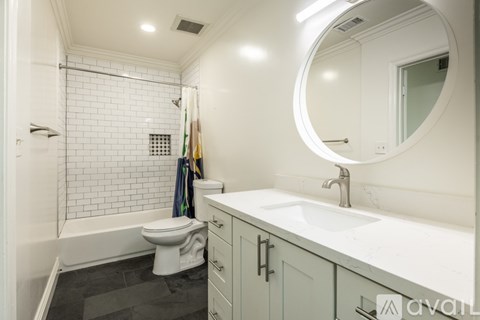 A bathroom with a toilet, sink, and a round mirror.