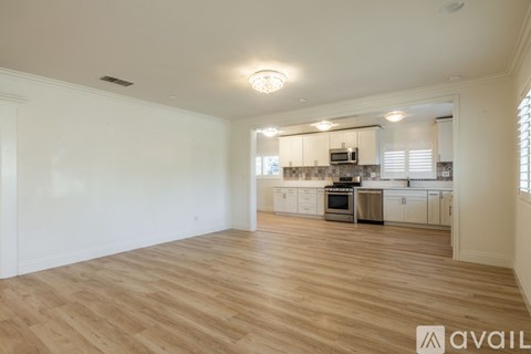 A spacious kitchen and living room with wooden flooring and white walls.
