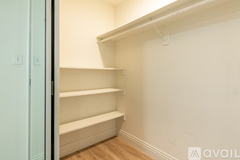 A room with a white wall and a wooden floor with a shelving unit.