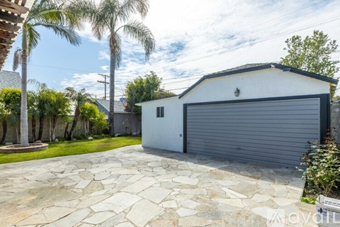 A white house with a grey garage door is surrounded by greenery.