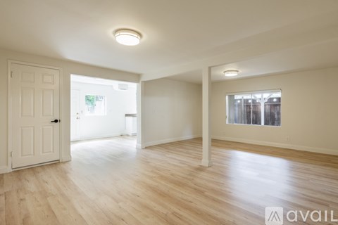 A spacious room with wooden flooring and white walls.
