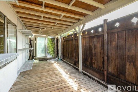 A wooden deck with a white railing and a glass door leading to a garden.