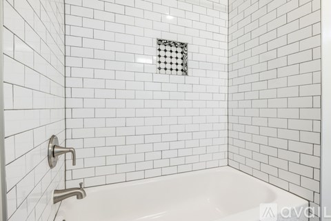 A white tiled bathroom with a white tub and a white shower head.