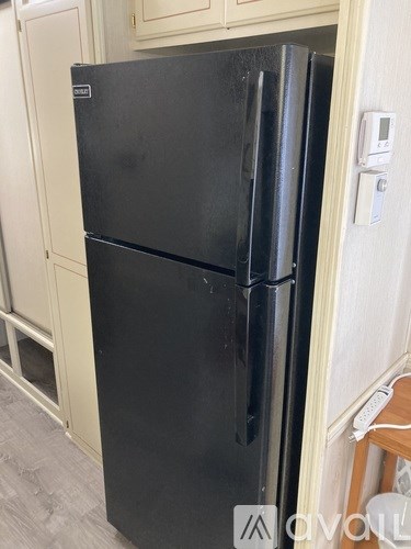 A black fridge in a kitchen with a white wall and a wooden stool.