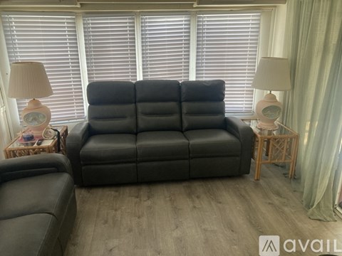 A black leather sofa sits in a room with wooden floors and two lamps on side tables.