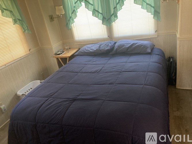 A bed with a blue comforter and two pillows sits in a room with a window.