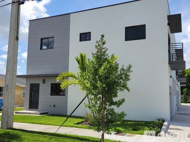 A white house with a grey roof and a tree in front.