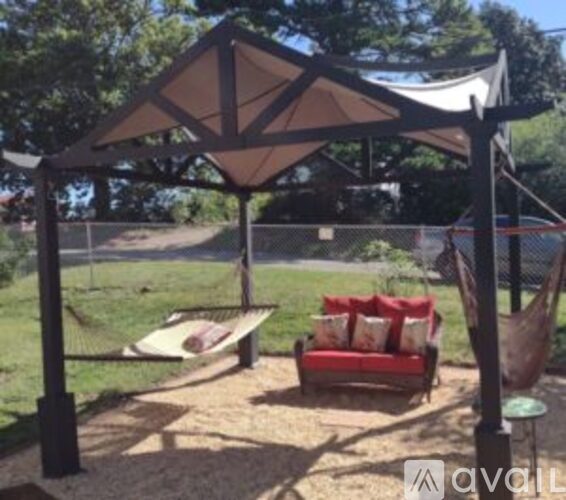 A gazebo with a red couch and pillows is set up in a grassy area.