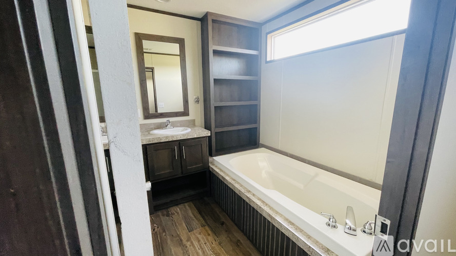 A bathroom with a tub, sink, mirror, and wooden floors.