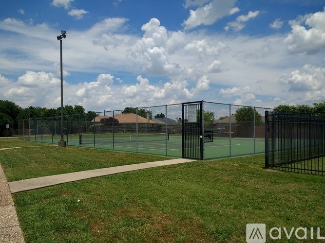 A tennis court surrounded by a fence and a walkway.