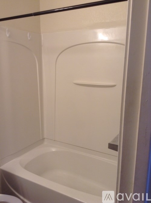 A white bathtub is in a bathroom with a black shelf above it.