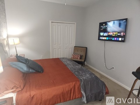 A bedroom with a bed, a chair, and a flat screen TV mounted on the wall.