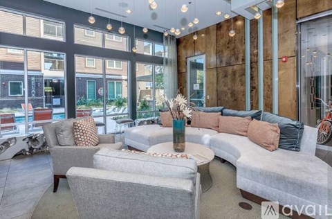 A living room with a grey sofa, a grey armchair, a grey ottoman, and a glass table with a vase on it.
