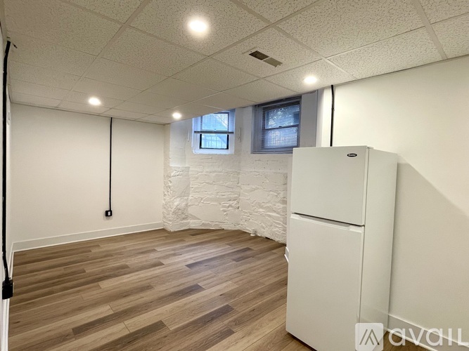 A room with a white fridge and wooden flooring.
