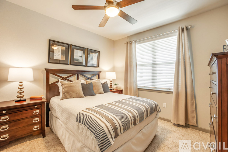 A well-lit bedroom with a large bed, a ceiling fan, and a nightstand with a lamp.
