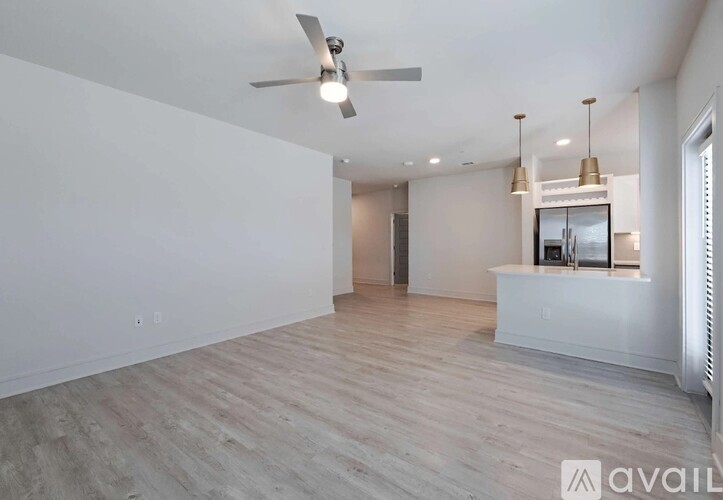 A spacious room with a ceiling fan and light, hardwood flooring, and a white wall with a window.