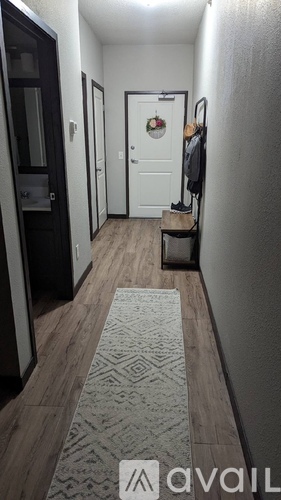 A hallway with a rug on the floor and a coat hanging on the door.