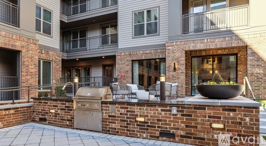 A brick patio with a grill and chairs is in front of a building.