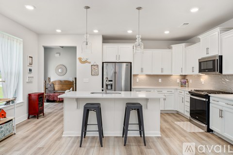 A kitchen with white cabinets and a large island with two black stools.