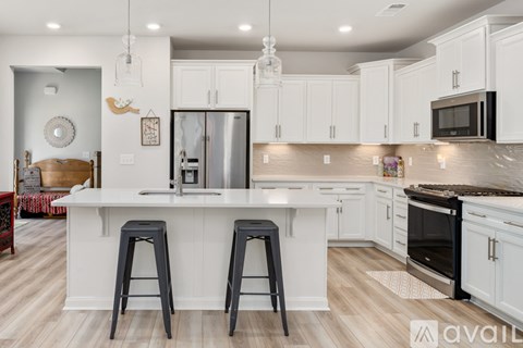 A kitchen with white cabinets and a white island with two black stools.