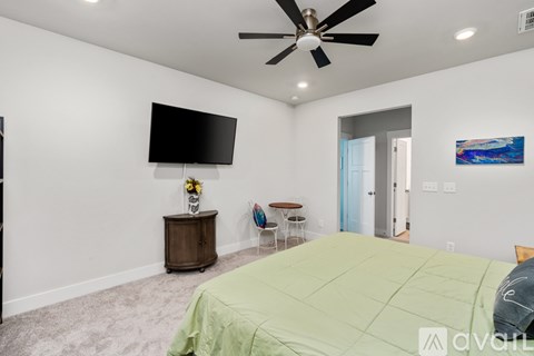 A bedroom with a bed, a ceiling fan, and a flat-screen TV mounted on the wall.