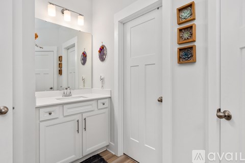 A white bathroom with a mirror, sink, and wall decorations.