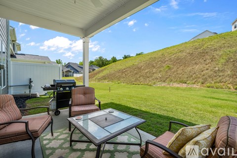 A patio with a glass table and chairs overlooking a grassy hill.
