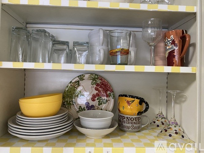 A kitchen cabinet with yellow and white checkered shelf paper and various dishes and glasses on the shelves.