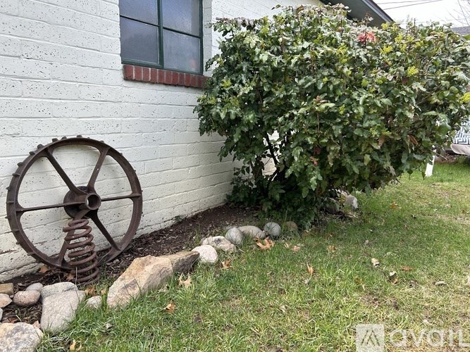 A white house with a red window and a bush next to it.