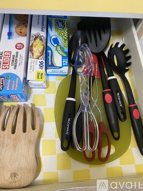 A set of kitchen utensils including a spatula, spoon, and tongs are displayed on a yellow and white checkered surface.