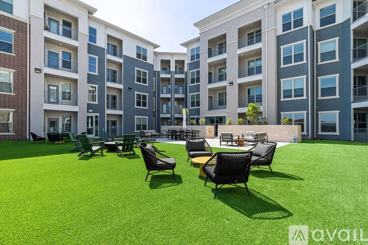 A grassy area with chairs and tables in front of apartment buildings.