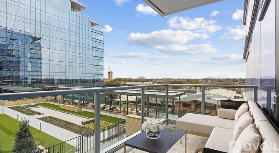 A modern balcony with a glass table and white couch overlooking a cityscape.