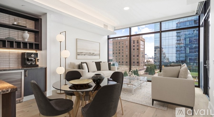 A modern living room with a glass table and chairs, a wooden cabinet, and a large window overlooking the city.