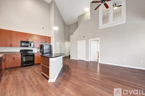 A spacious living room with hardwood floors and a kitchen area with a black stove top oven.