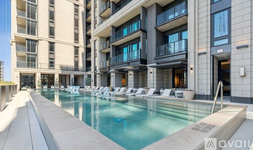 A large, modern pool area with lounge chairs and apartment buildings in the background.