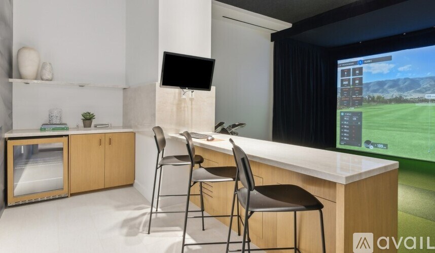 A modern room with a desk, chairs, and a large screen displaying a golf course.