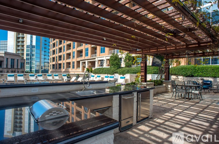 A wooden pergola over a table with chairs and a barbecue grill.